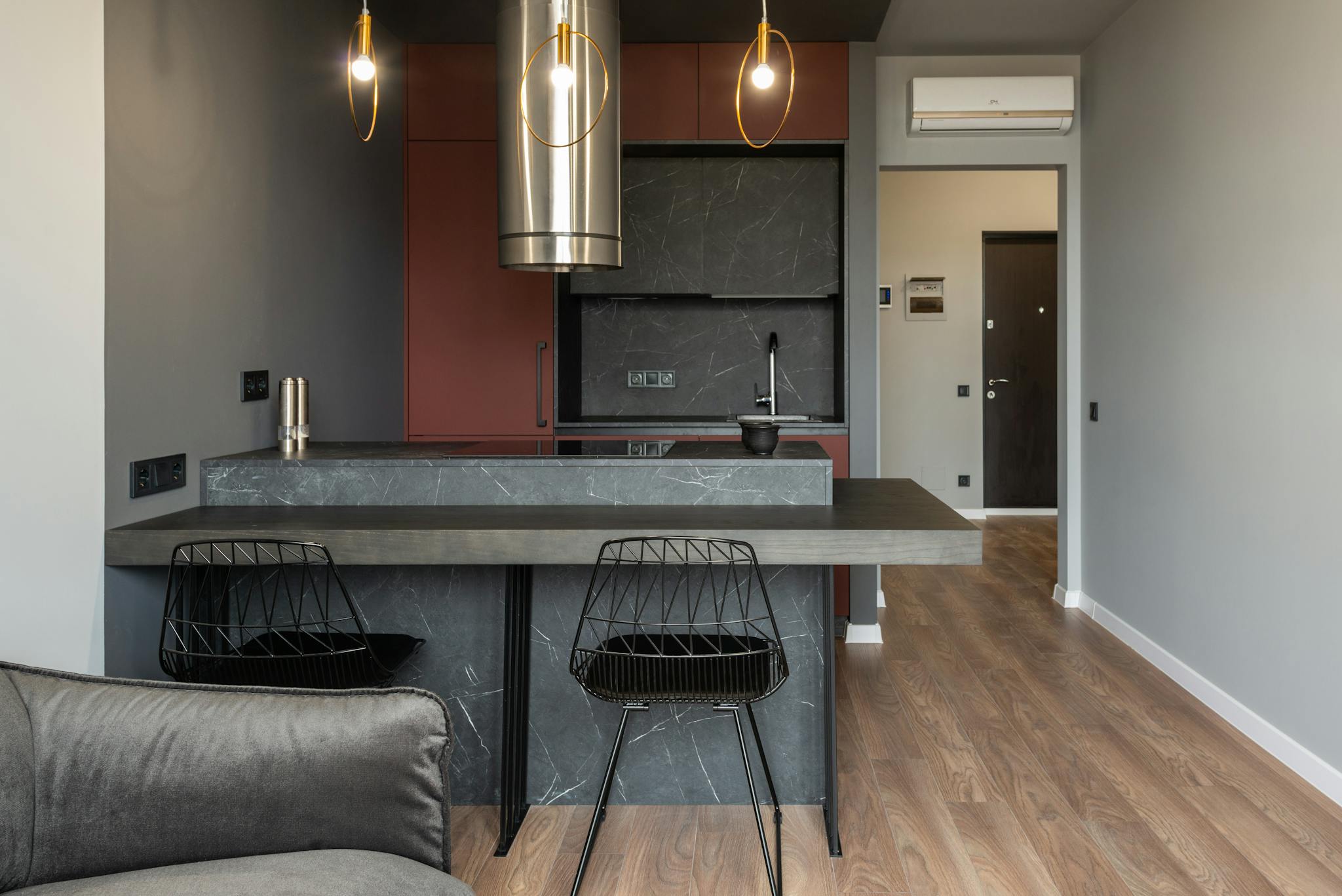 Dining zone furnished with counter and chairs in modern apartment with island style kitchen equipped with range hood and illuminated by hanging lamps