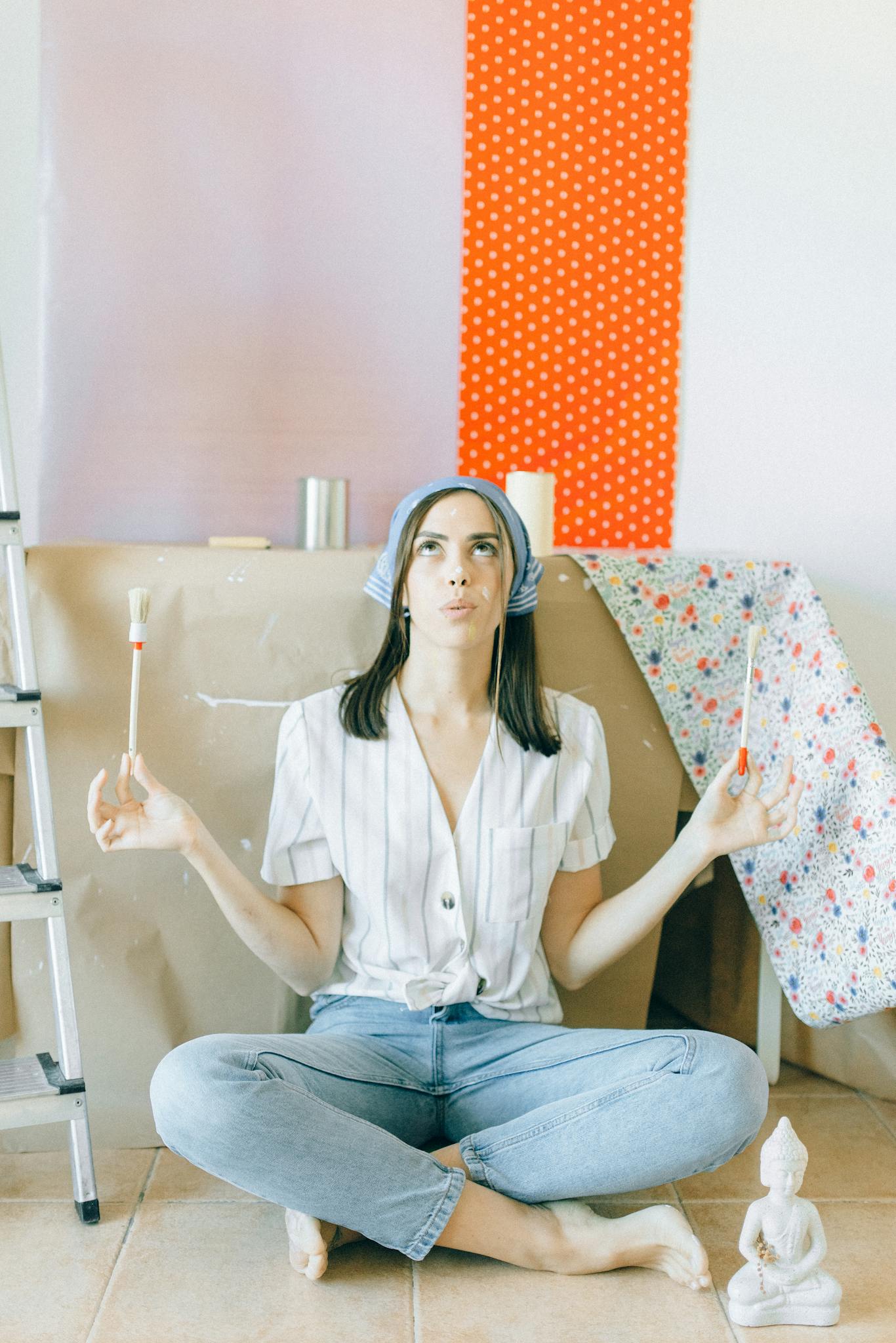 Young woman meditates while sitting among painting supplies, embracing creativity at home.